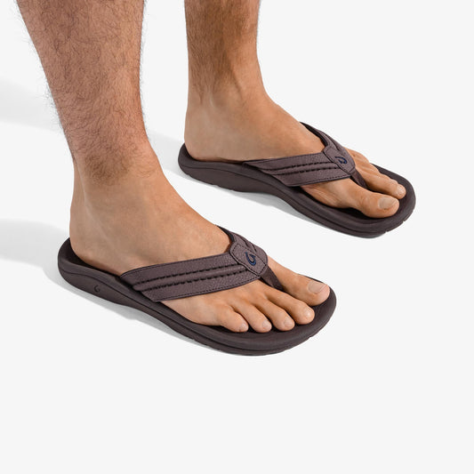 Dark brown thong sandals with padded straps worn by a man on white background.