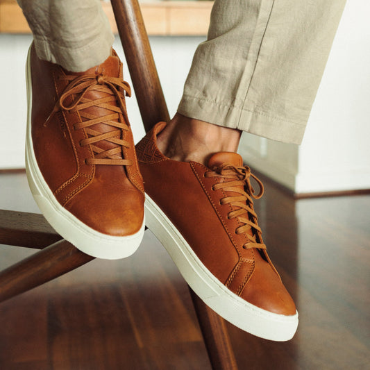 Cognac leather lace-up sneakers with white sole, worn with beige pants.