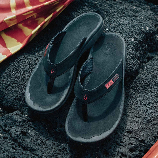 Black thong flip-flops with red accent details and logo patch on textured sole.