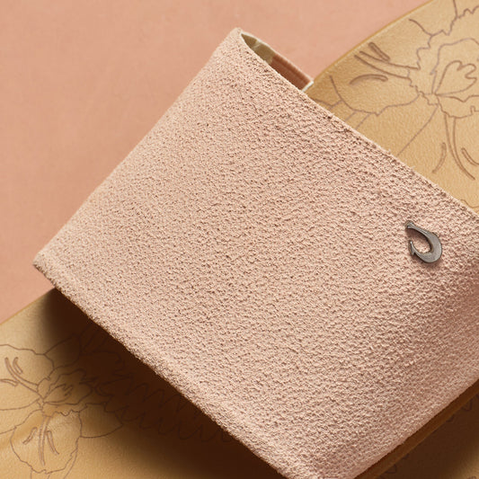 Soft pink textured pouch with small metal hook detail on warm sand patterned background.