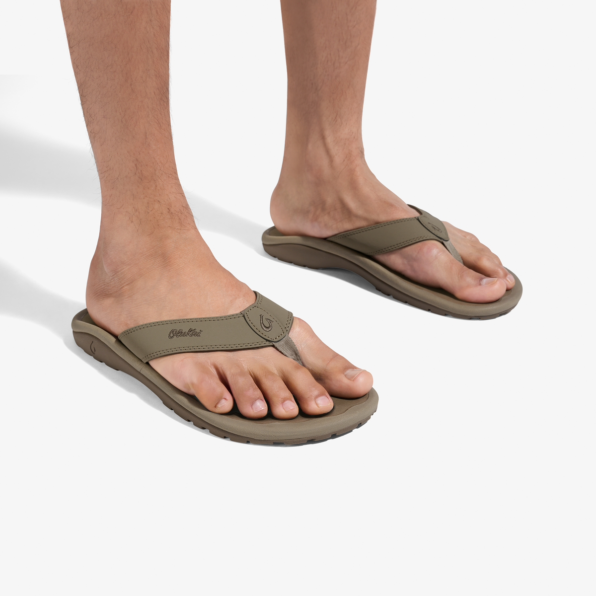 Tan thong sandals with curved straps worn on bare feet.