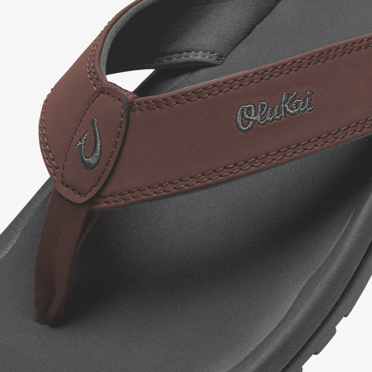 Close-up of burgundy leather thong sandal strap with embroidered branding on gray sole.