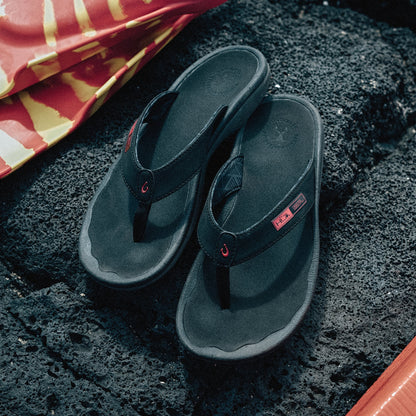 Black thong flip-flops with gray soles and red accent details on textured dark surface.