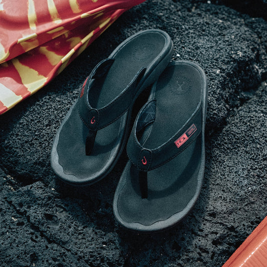 Black thong flip-flops with gray soles and red accent details on textured dark surface.