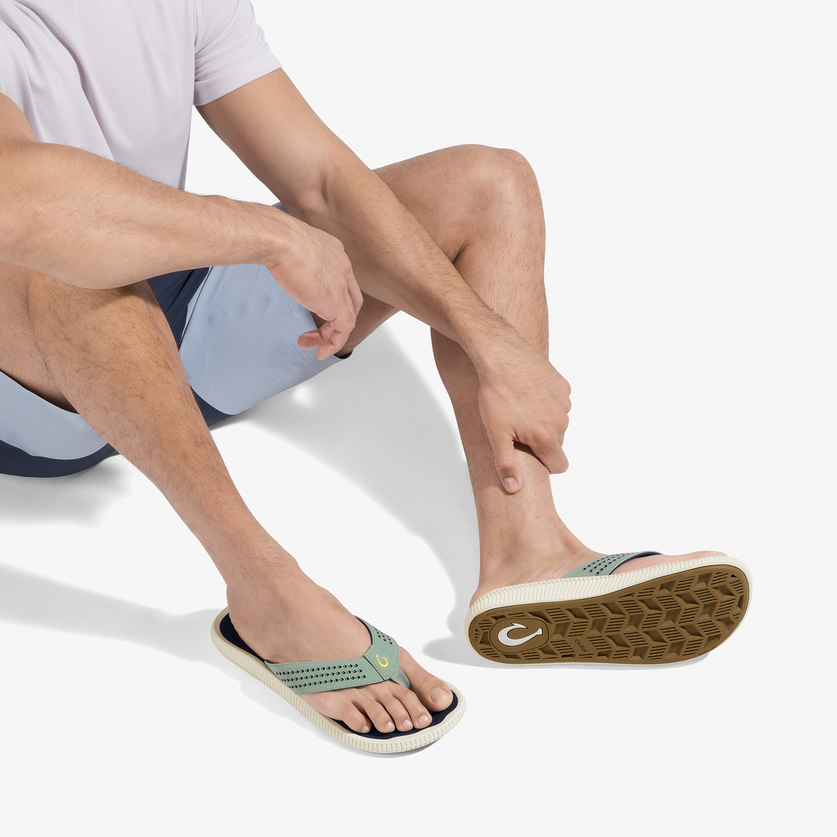 Man wearing seagreen and navy sandals with perforated upper and textured sole, shown from below while seated.