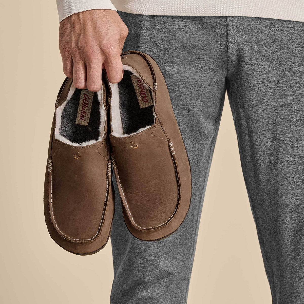 Brown leather slippers with black and white fleece lining, held in hand, showing rounded toe and stitched seams.
