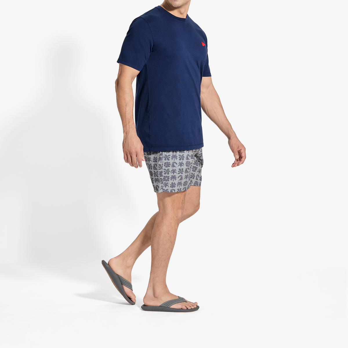 Man wearing navy crew-neck t-shirt with patterned shorts and dark sandals.