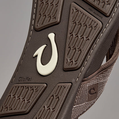 Dark brown shoe sole with cream-colored hook detail and textured tread pattern.