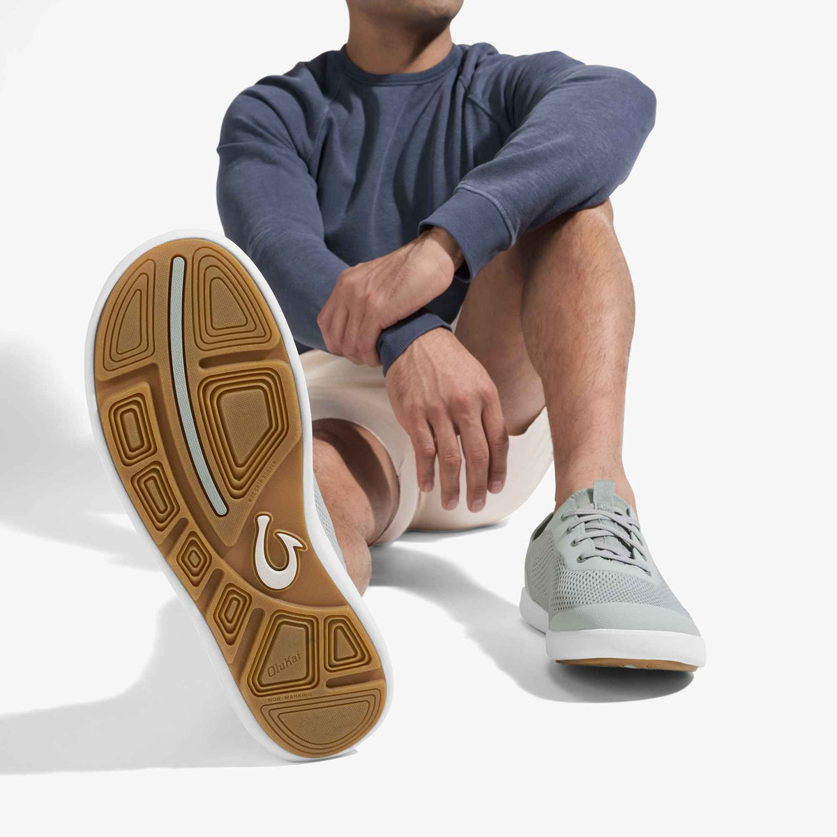 Grey sneaker with white and tan sole, worn with blue long-sleeve shirt and light shorts.