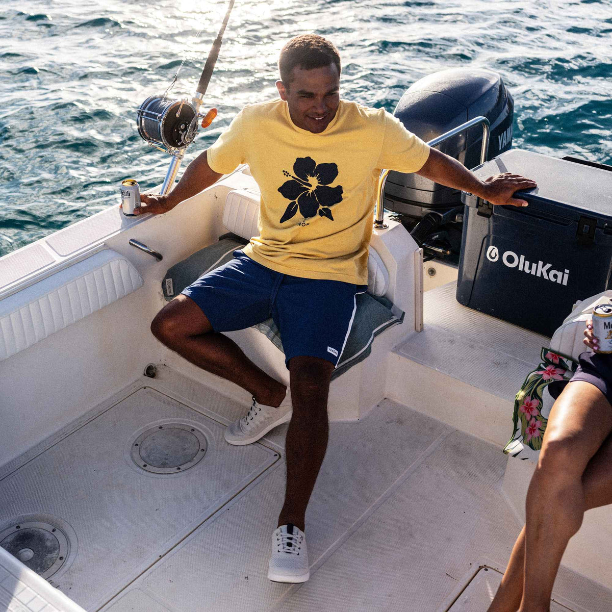 Man wearing white sand and trench blue swim shorts on a boat deck with ocean background.