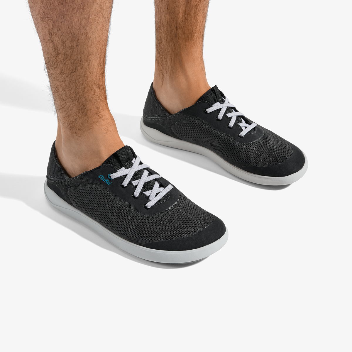 Black mesh sneakers with white laces and gray soles worn on male feet.