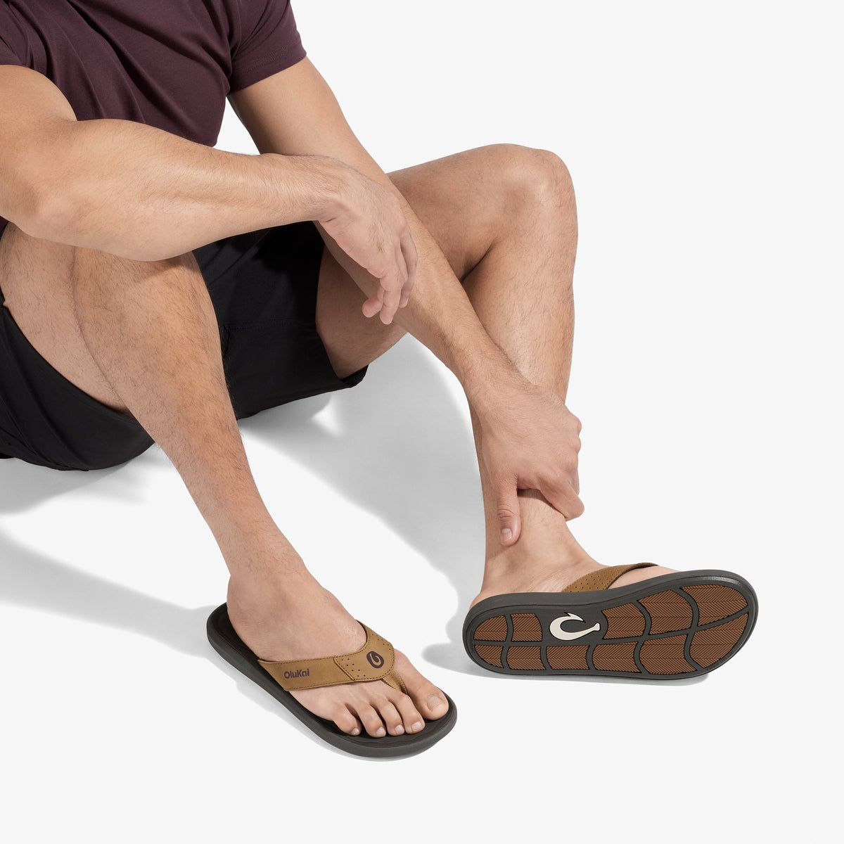 Man wearing tan and black thong sandal with textured sole, shown from ankle down while seated.