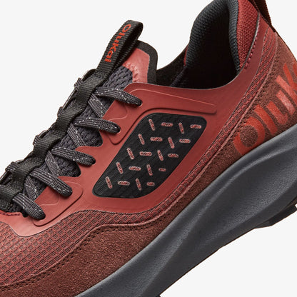 Red clay and carob athletic shoe with black laces, perforated panels, and gray sole detail.