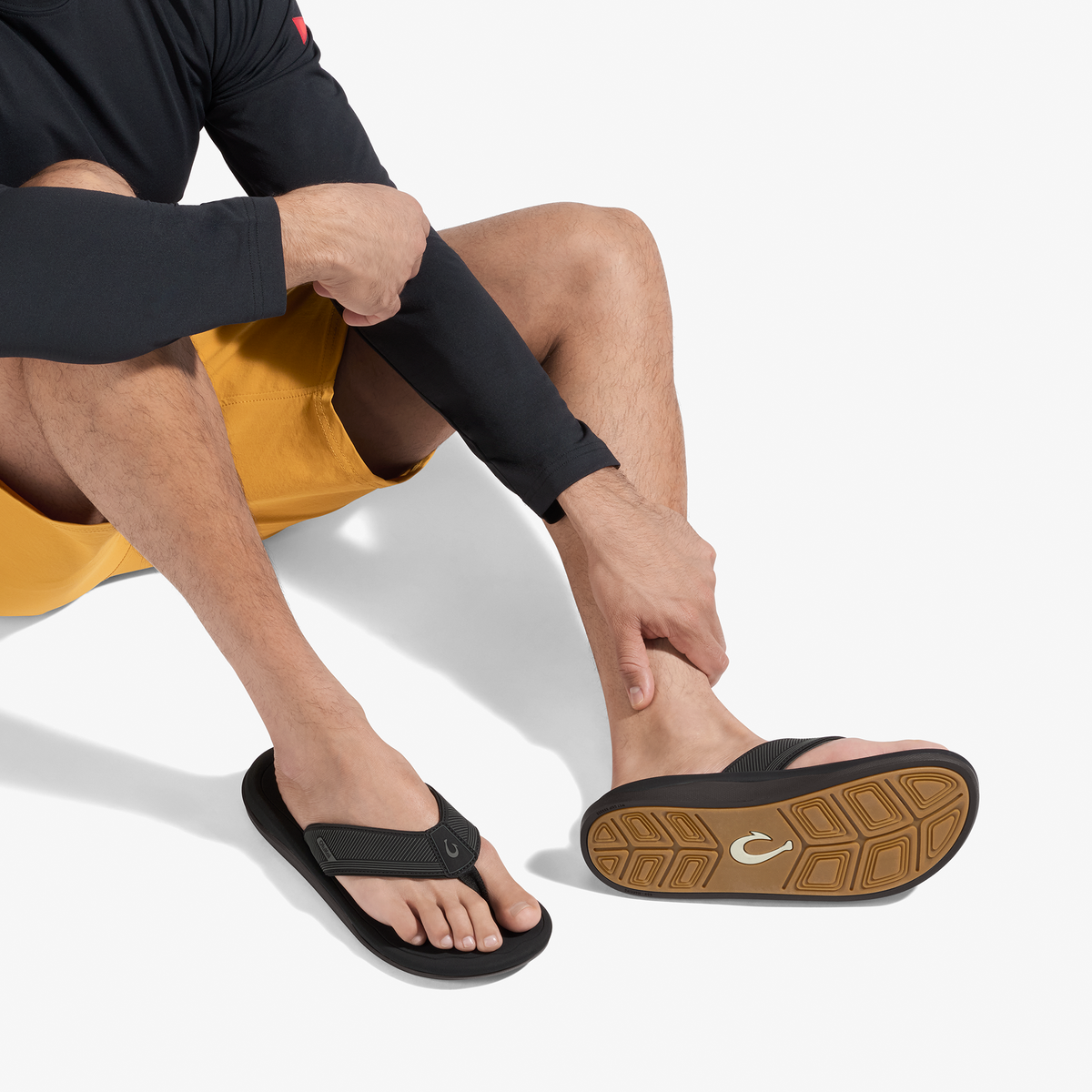 Man wearing black long-sleeve rashguard, yellow swim shorts, and black flip-flops with tan sole.