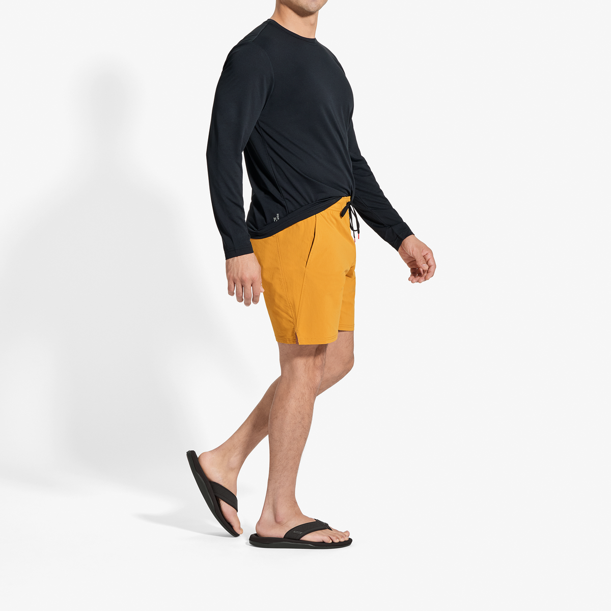 Man wearing black long-sleeve rash guard and yellow swim shorts with black sandals.