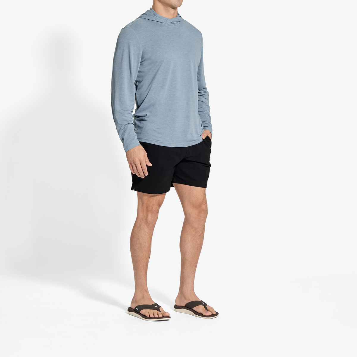 Man wearing light blue hooded long-sleeve shirt with black shorts and black sandals.
