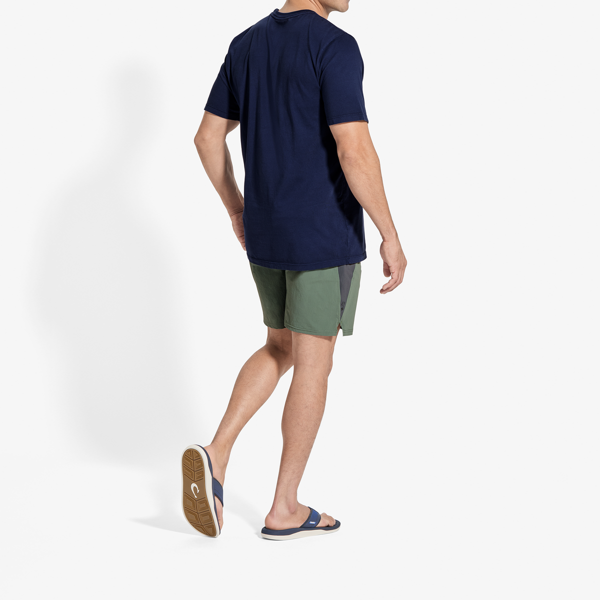 Man wearing navy short-sleeve t-shirt and olive green shorts with navy slide sandals, shown from behind.