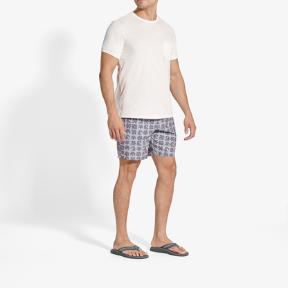 Man wearing white short-sleeve t-shirt and grey patterned shorts with dark slide sandals.
