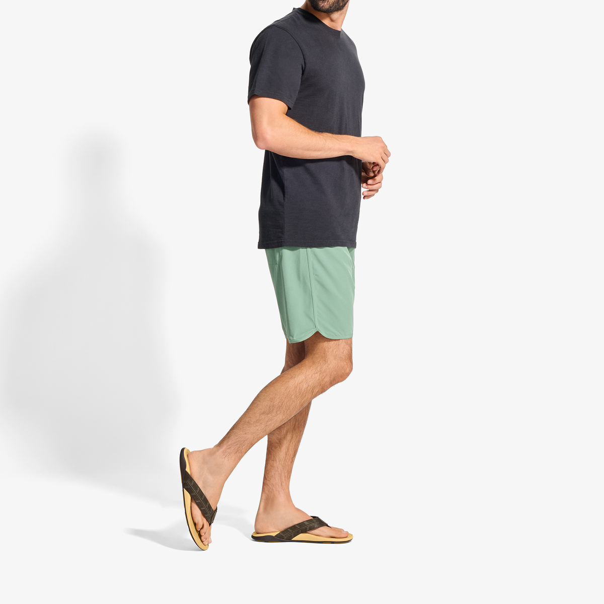 Man wearing dark navy t-shirt, light green shorts, and black and tan flip-flops, standing in profile.
