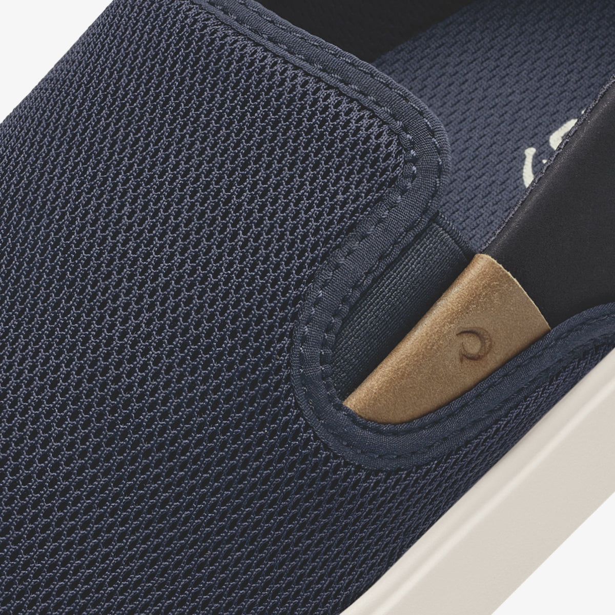 Dark blue textured slip-on shoe with tan leather heel patch and white sole.