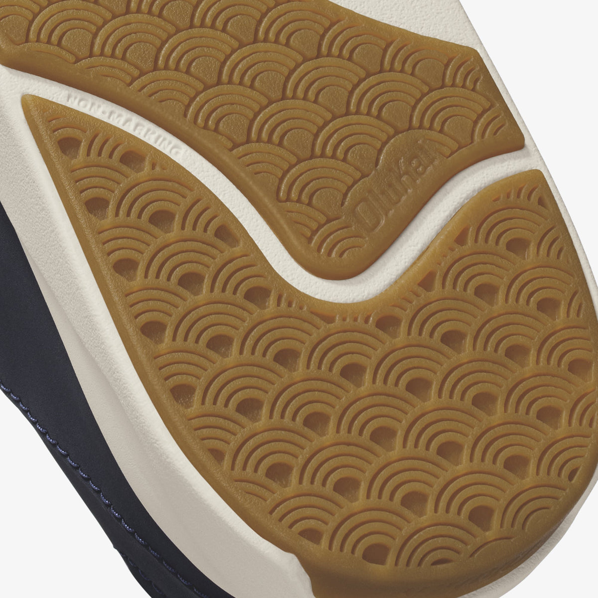 Tan shoe sole with geometric arc pattern, white midsole, and dark blue upper visible at edge.