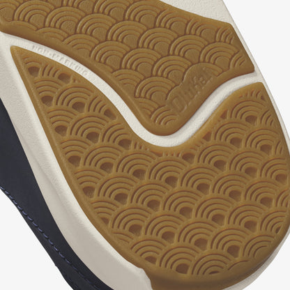 Tan shoe sole with geometric arc pattern, white midsole, and dark blue upper visible at edge.