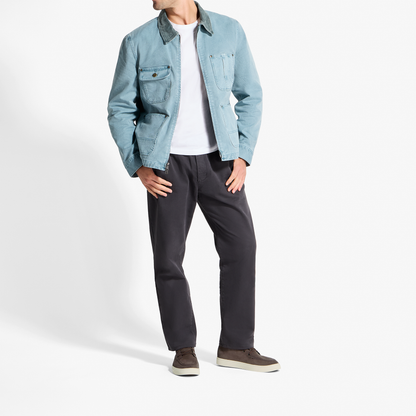 Man wearing light blue denim jacket, white t-shirt, black pants, and dark brown chukka boots.