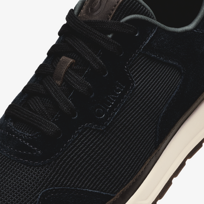 Black lace-up sneaker with textured mesh upper, dark suede accents, and cream-colored sole.