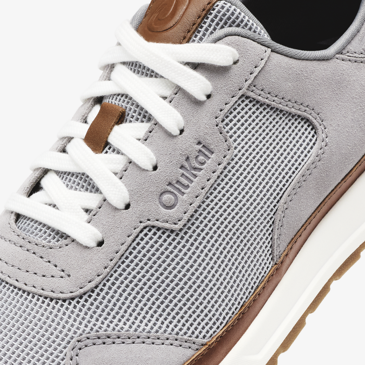 Light grey sneaker with brown heel tab, white laces, and textured mesh panels.