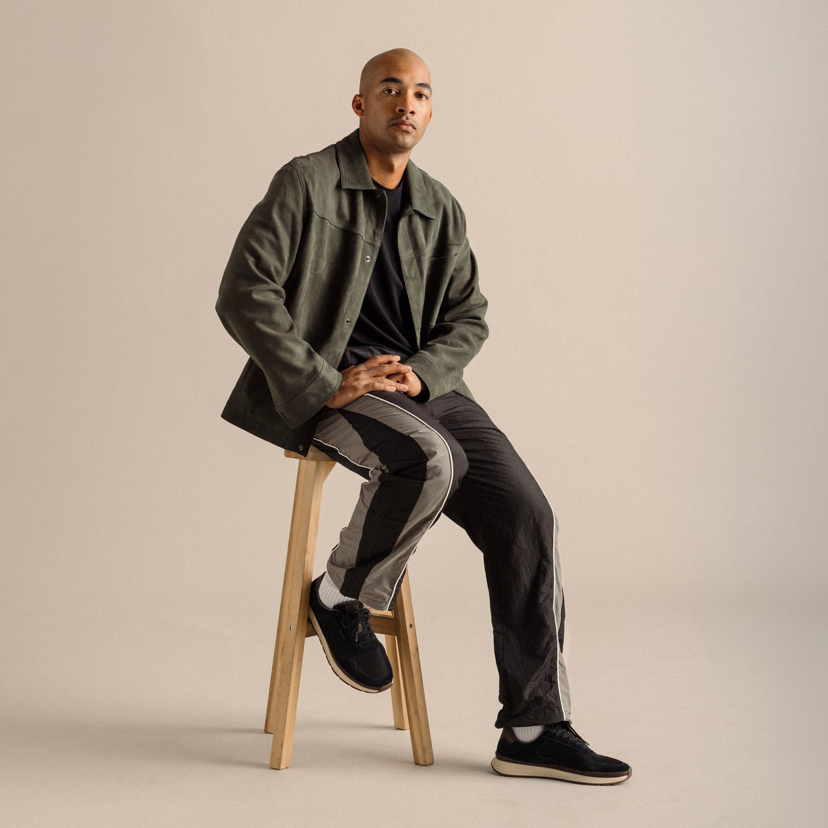 Black suede shoes with cream-colored sole and trim on a wearer styled with black shirt and olive jacket.