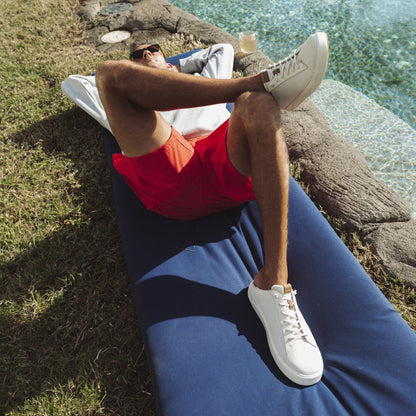 White canvas sneaker with lace-up closure worn by person sitting outdoors near water.