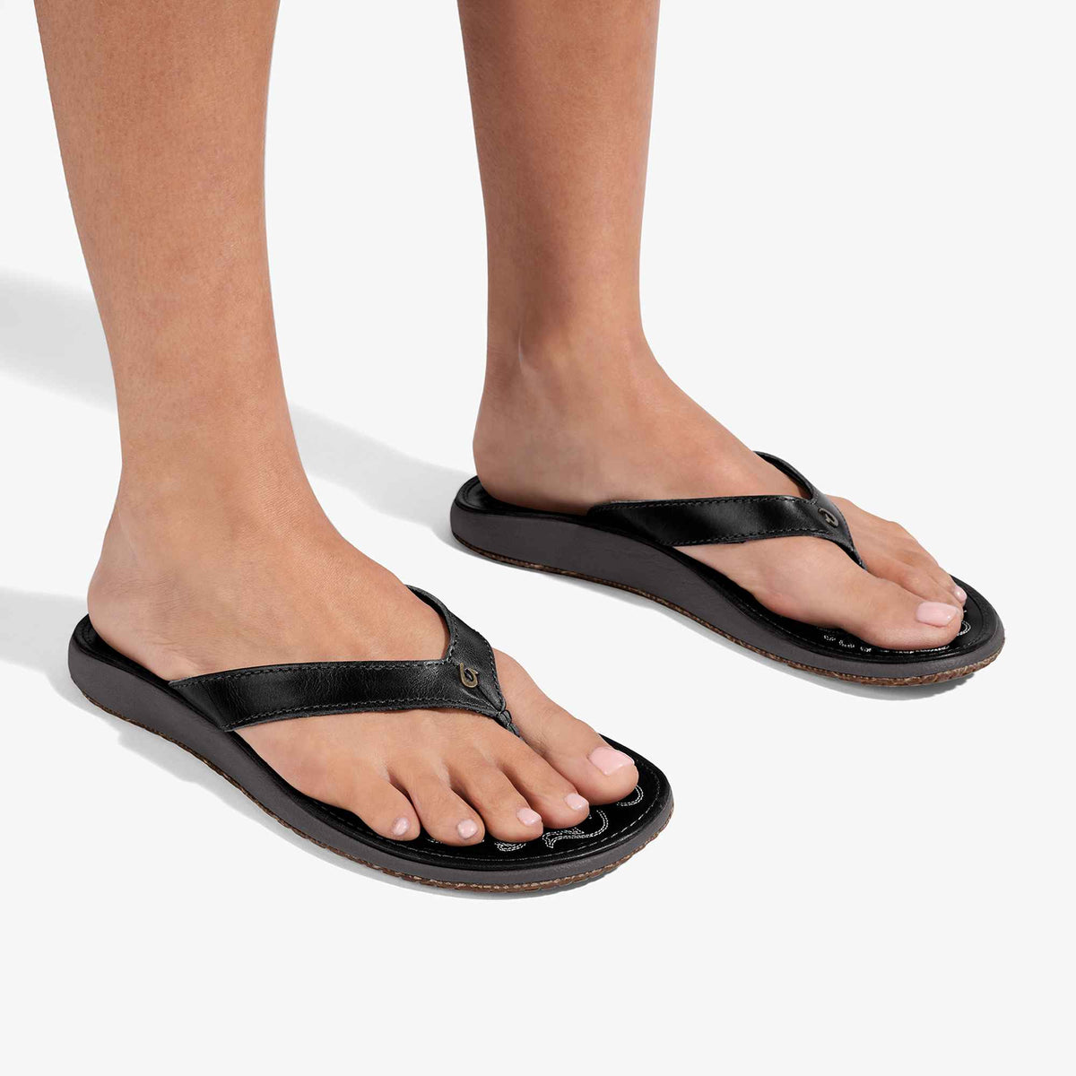 Black thong sandals with contoured footbeds worn on bare feet.