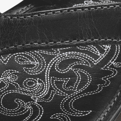 Black leather boot with white embroidered scrollwork design and contrasting stitching detail.