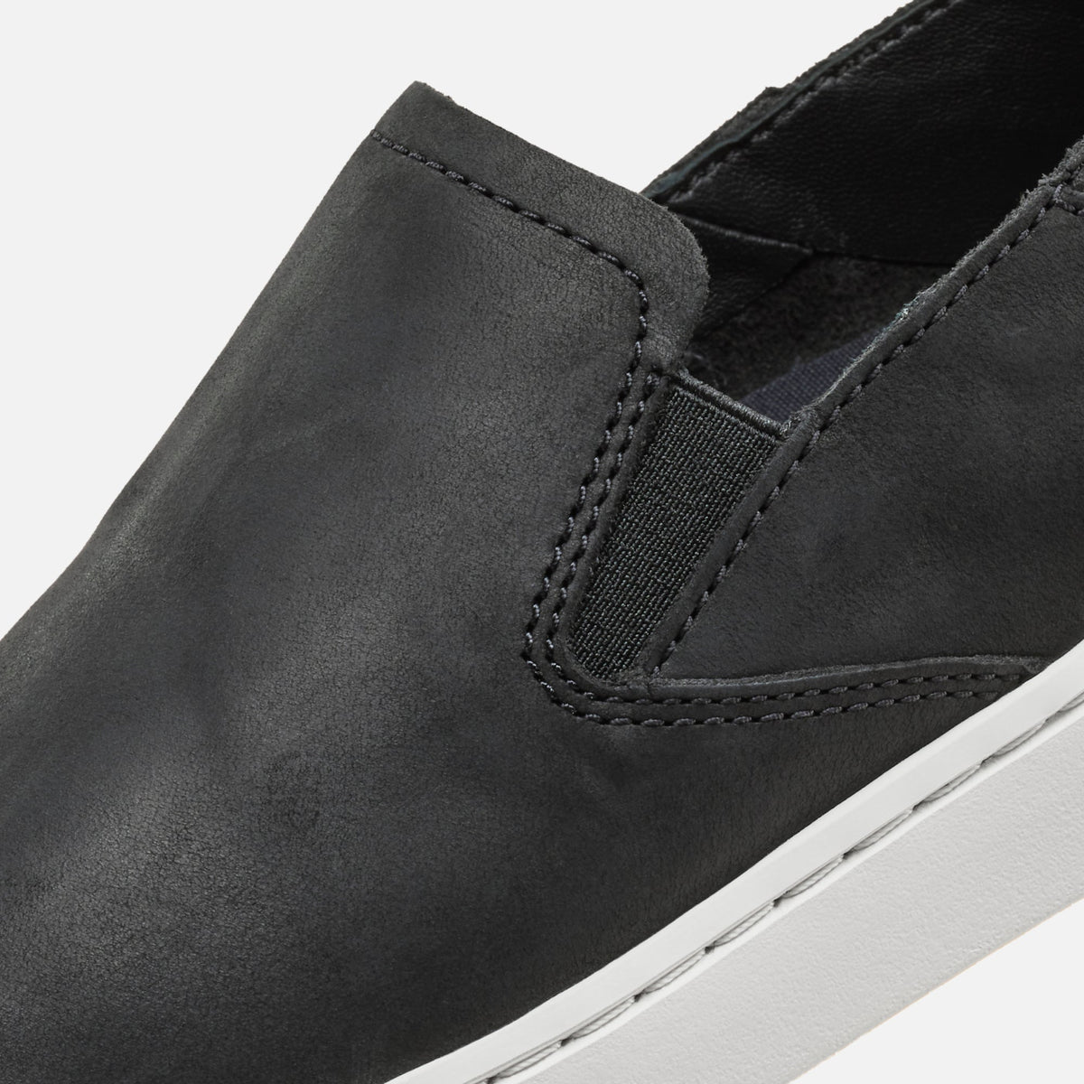 Black leather slip-on shoe with elastic gore detail and white sole, shown in close-up side view.