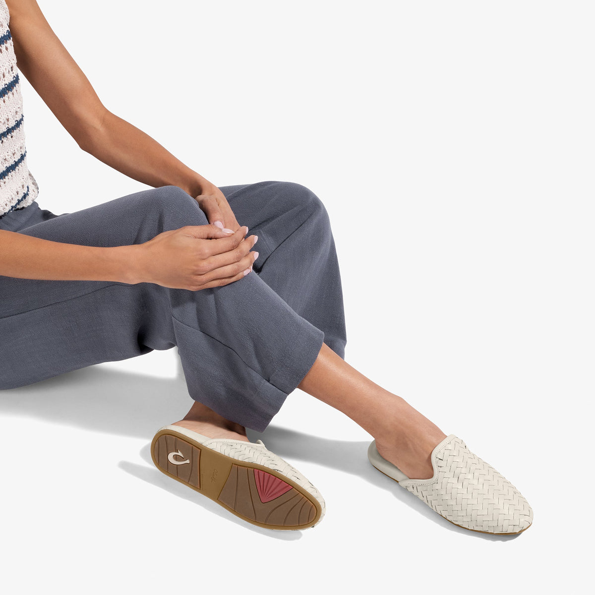 Person wearing cream woven slip-on shoes with brown sole and pink accent, paired with dark gray pants.