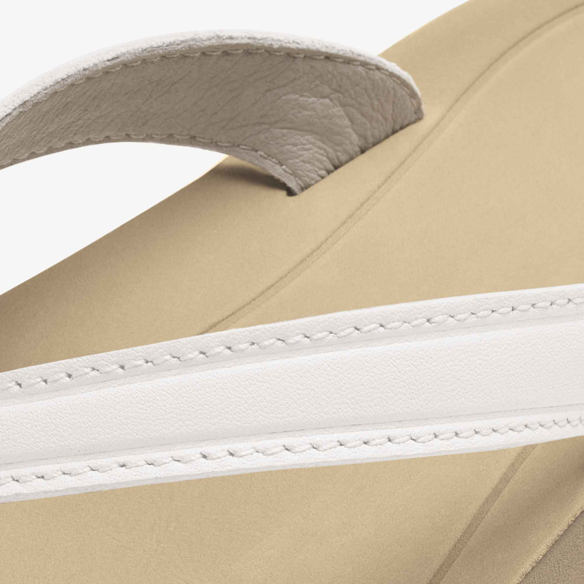 Close-up of sandal strap showing bright white top strap with stitching and warm sand-colored upper band with gray lining.