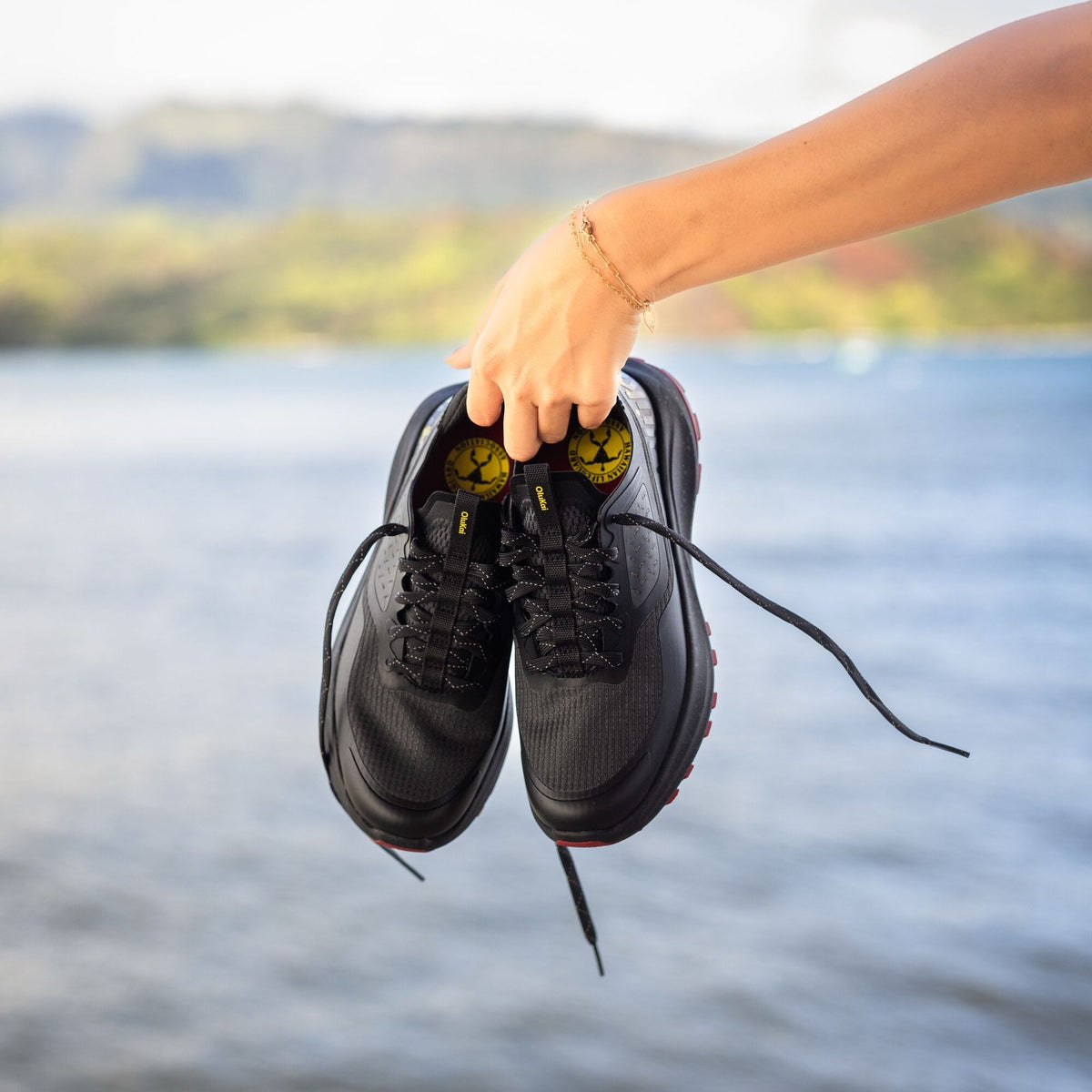 Black lace-up athletic shoes with yellow accents held in hand against water background.