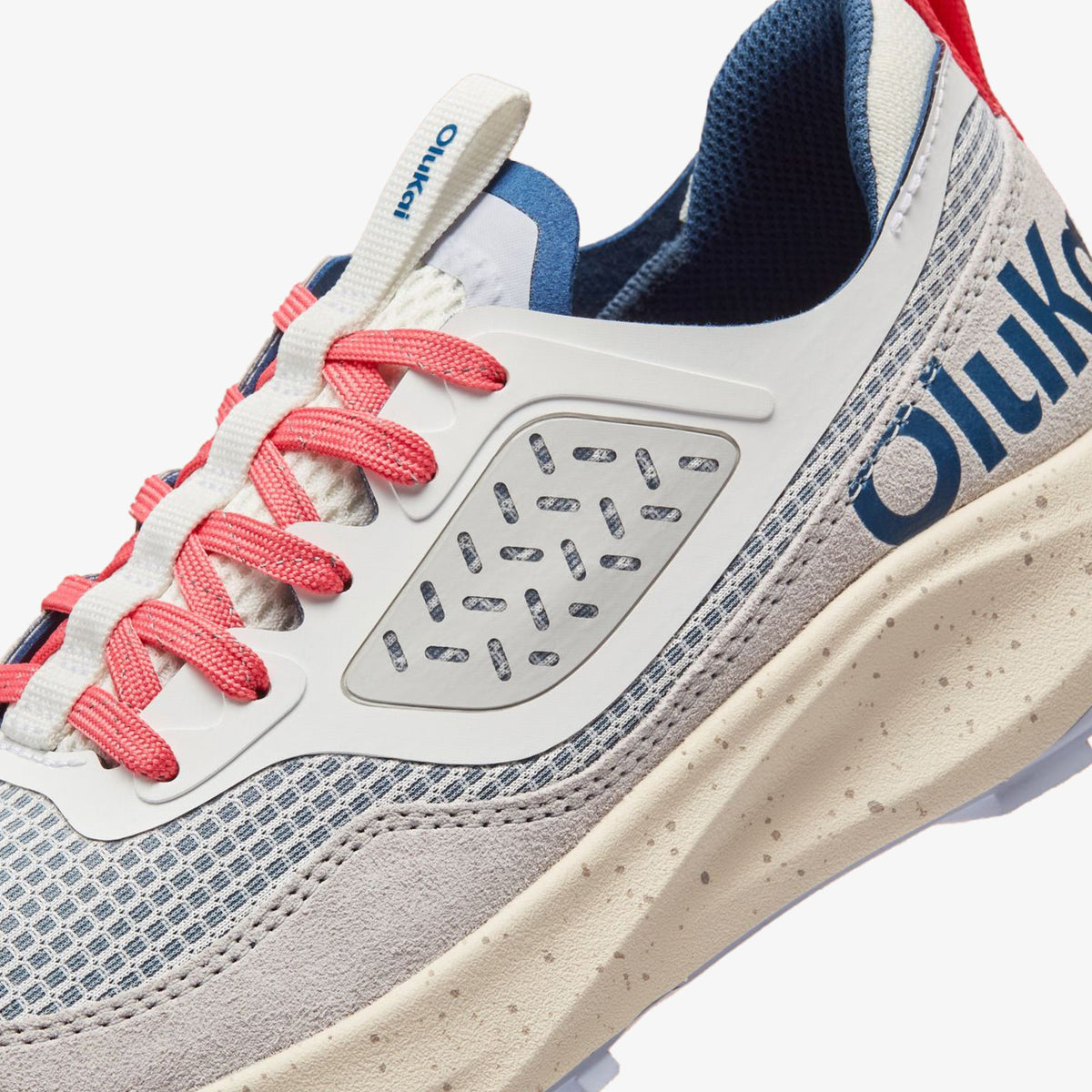 White sneaker with coastal blue mesh panels, red laces, perforated toe box, and cream-colored sole detail.