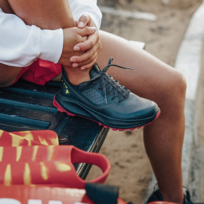 Black and pink trail running shoe with textured upper and lace closure worn with red patterned socks.