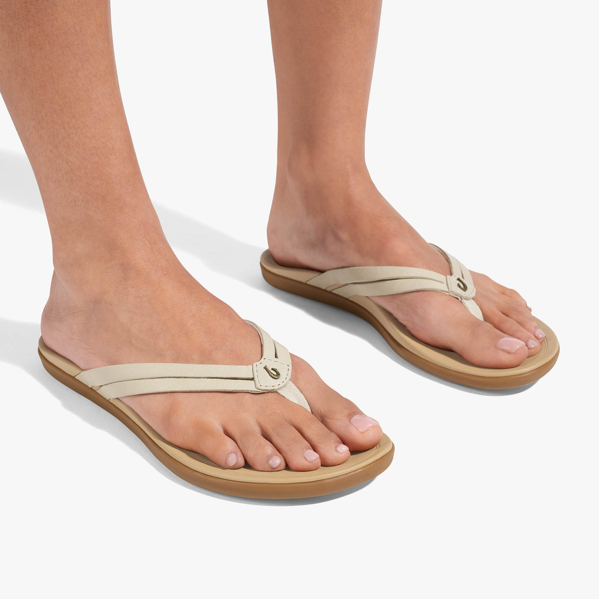Cream-colored flip-flop sandals with thong straps and tan rubber soles worn on bare feet.