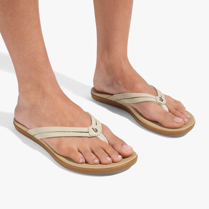 Cream-colored flip-flop sandals with thong straps and tan rubber soles worn on bare feet.