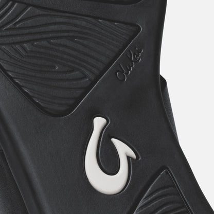 Black sandal with white hook detail and textured upper strap design.