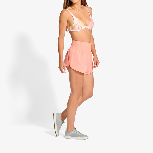 Woman wearing pink bikini top with white polka dots and matching pink ribbed skirt with grey sneakers.