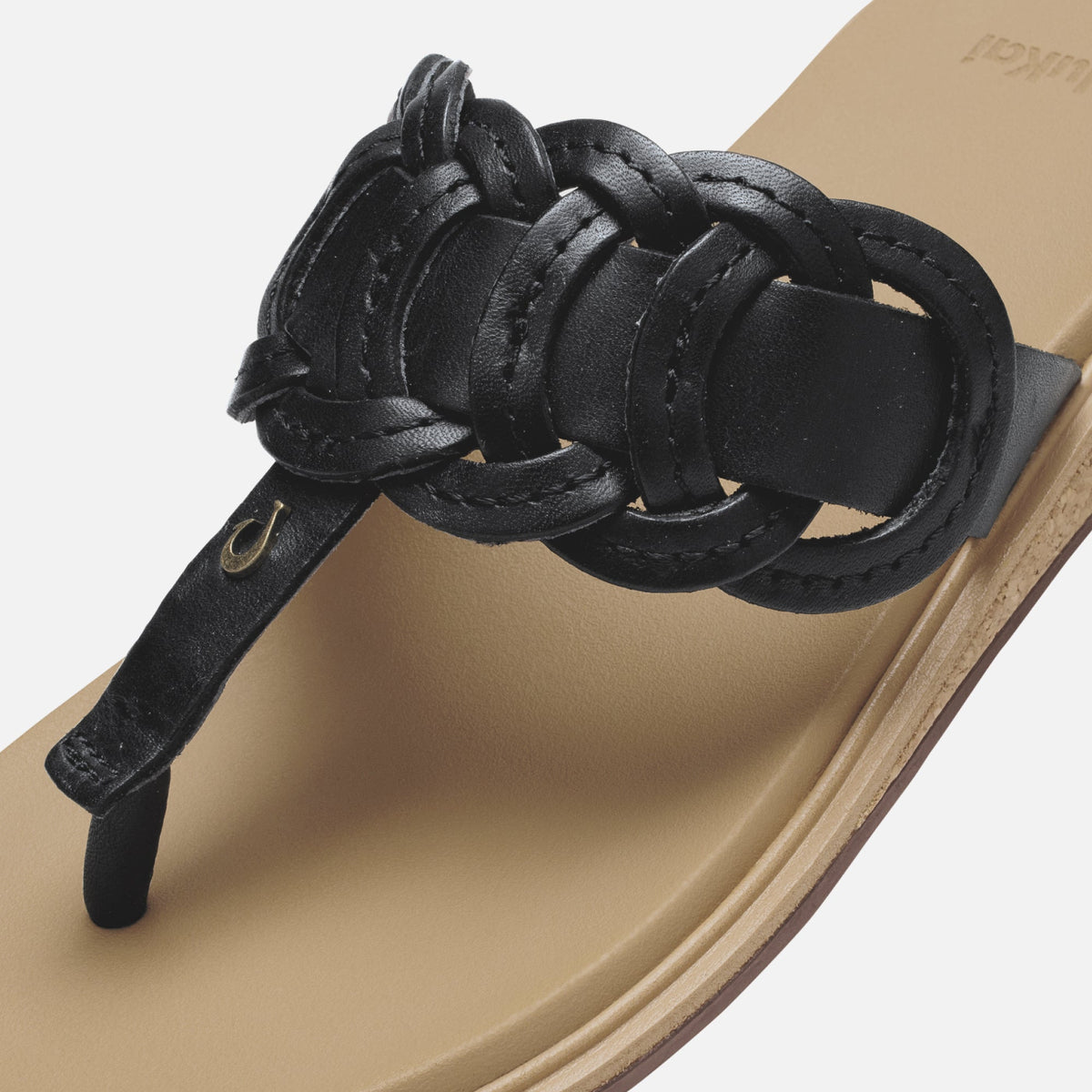 Black leather sandal with knotted toe strap detail on warm sand-colored sole.