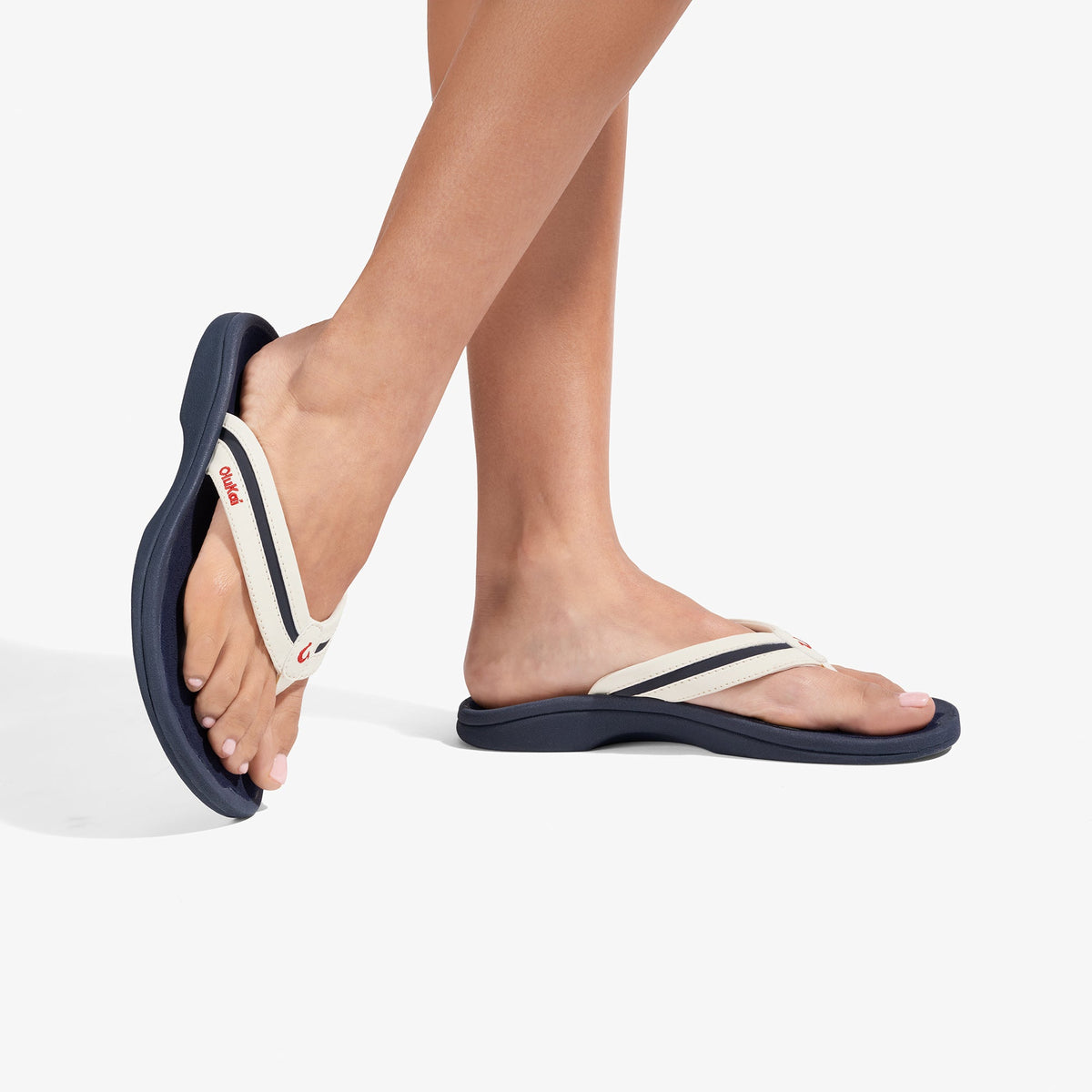 White and navy thong sandals with cushioned soles shown worn on a person's feet.
