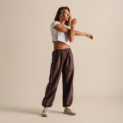 Woman wearing white cropped t-shirt and brown elastic-waist pants with cream sneakers.
