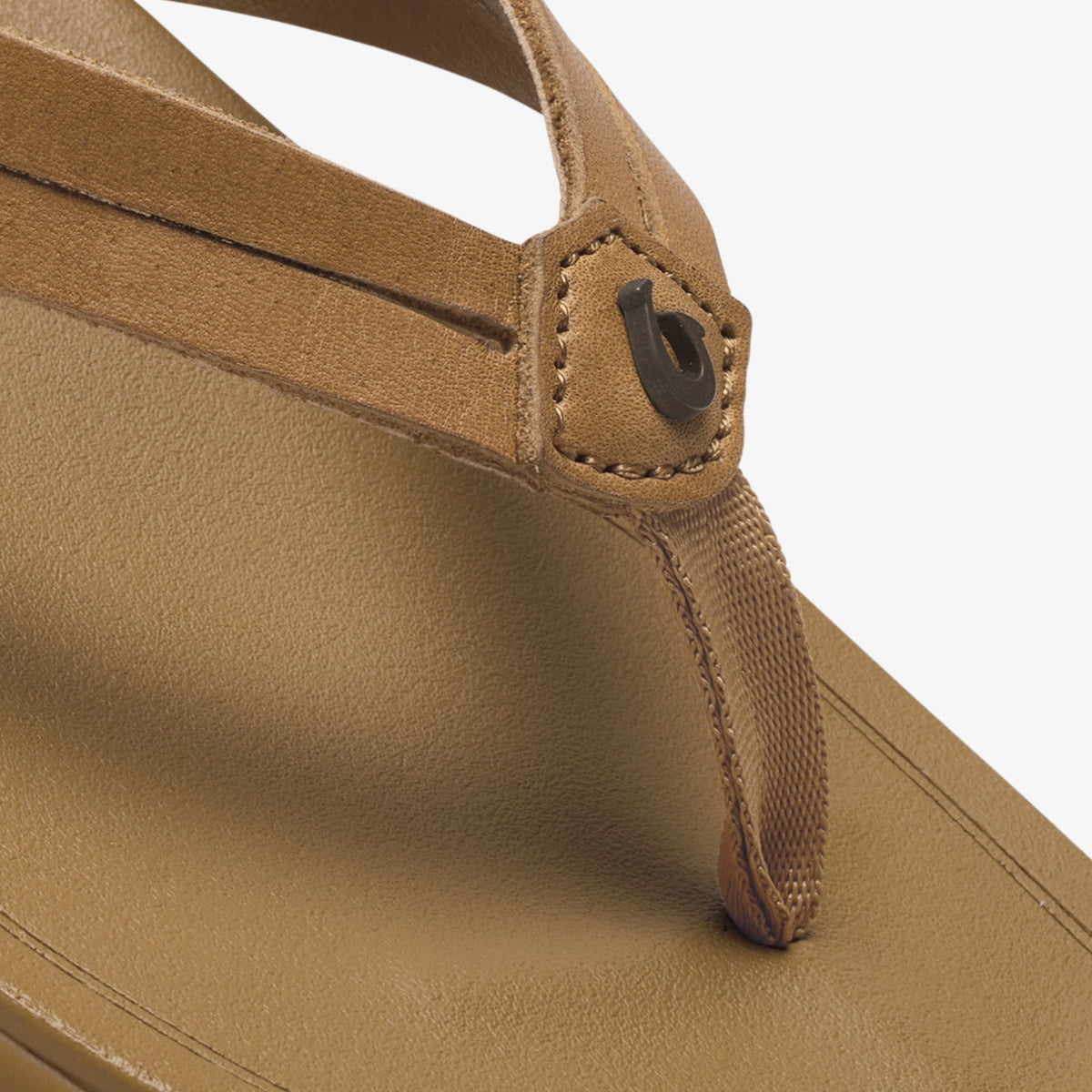 Tan suede flip-flop with dark button detail at toe post and woven ankle strap.